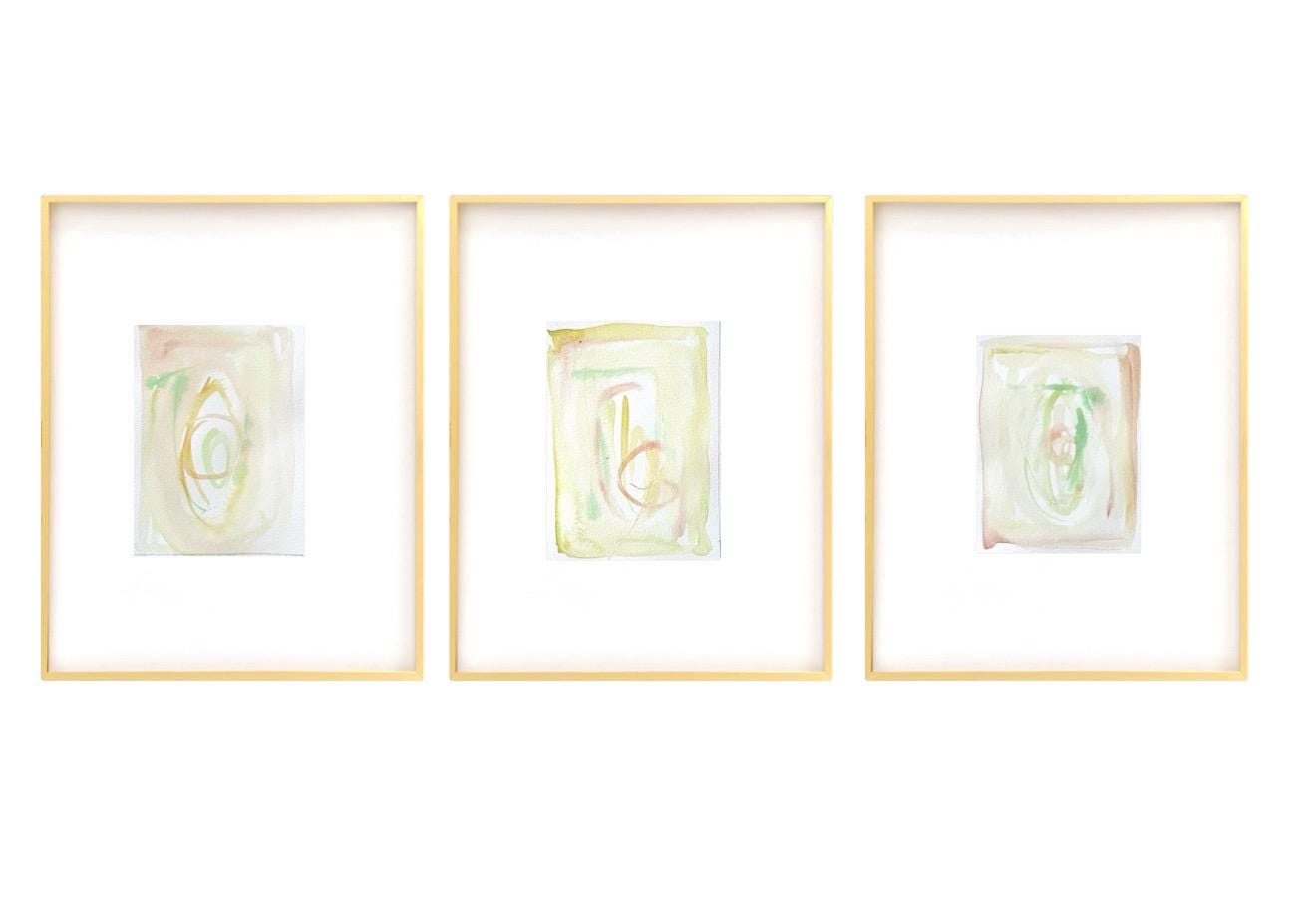 Set of three framed abstract watercolor paintings with pastel turquoise, pink, green, and yellow hues in white mats and gold frames.