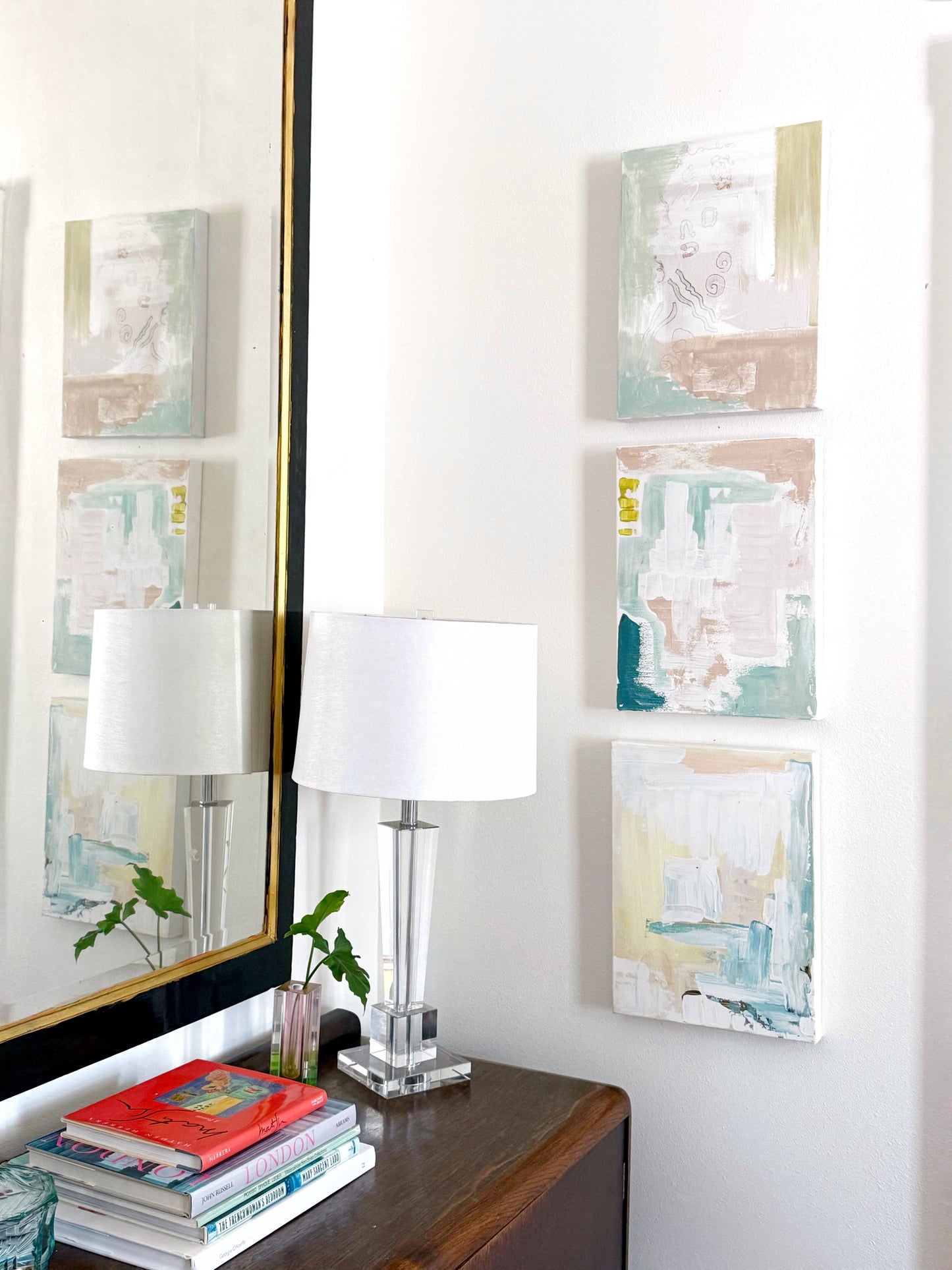 Original abstract mixed media paintings on 16x20 stretched canvas displayed on white wall above wooden table with lamp and books