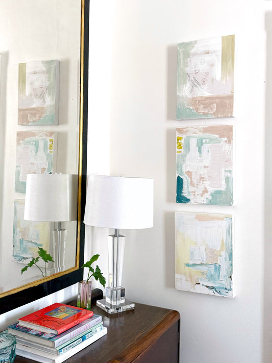 Original abstract mixed media paintings on 16x20 stretched canvas displayed on white wall above wooden table with lamp and books