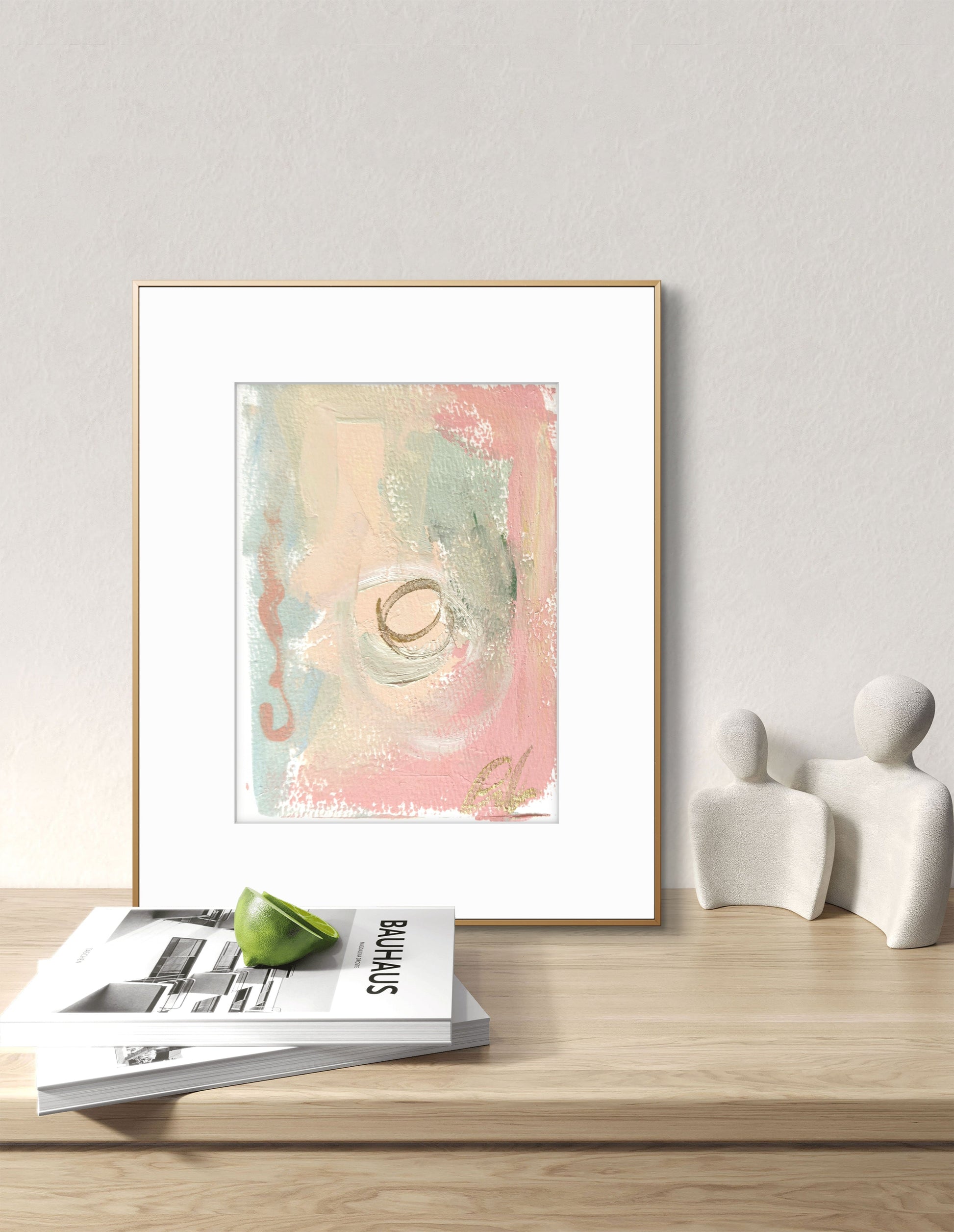 Original abstract watercolor painting fine art print in blue, peach, and pink tones, framed and displayed on a desk with decorative objects