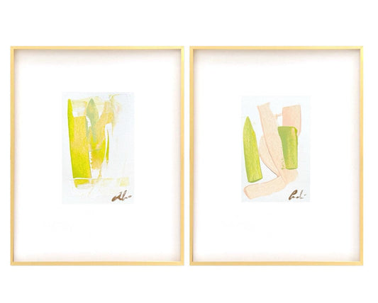 Pair of abstract watercolor paintings in pink, green, and peach hues, matted in white and framed in gold.